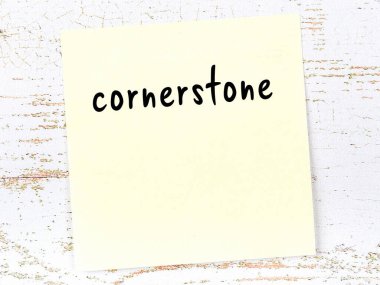 Concept of reminder about cornerstone. Yellow sticky sheet of paper on wooden wall with inscription