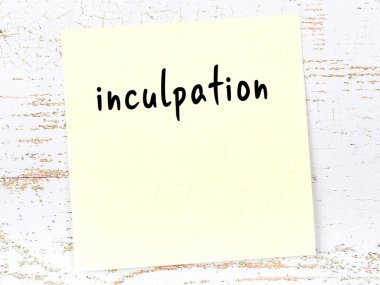 Yellow sticky note on wooden wall with handwritten inscription inculpation