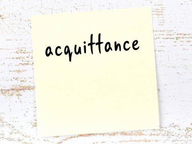 Yellow sticky note on wooden wall with handwritten inscription acquittance