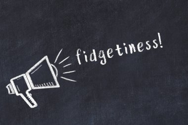 Chalk drawing of loudspeaker and handwritten inscription fidgetiness on black desk