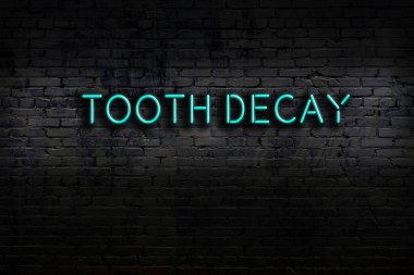 Neon sign on brick wall at night. Inscription tooth decay