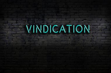 Neon sign with inscription vindication against brick wall. Night view