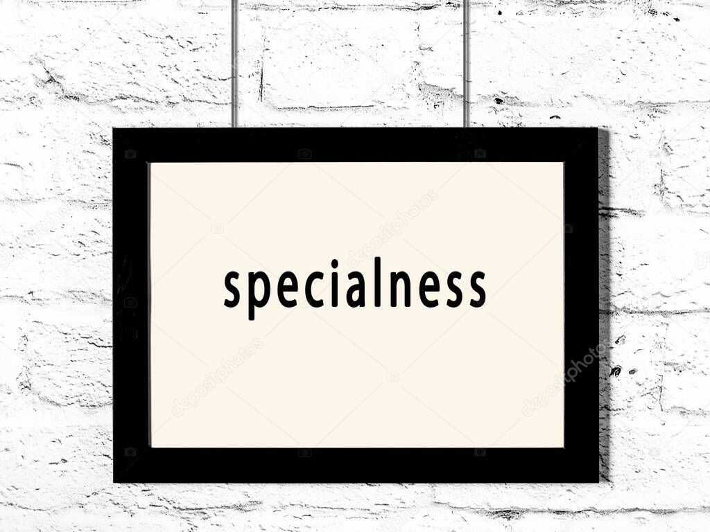 Black wooden frame with inscription specialness hanging on white brick wall 