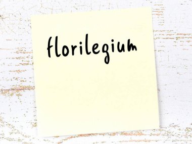 Tahta duvardaki sarı yapışkan notta el yazısı florilegium var.