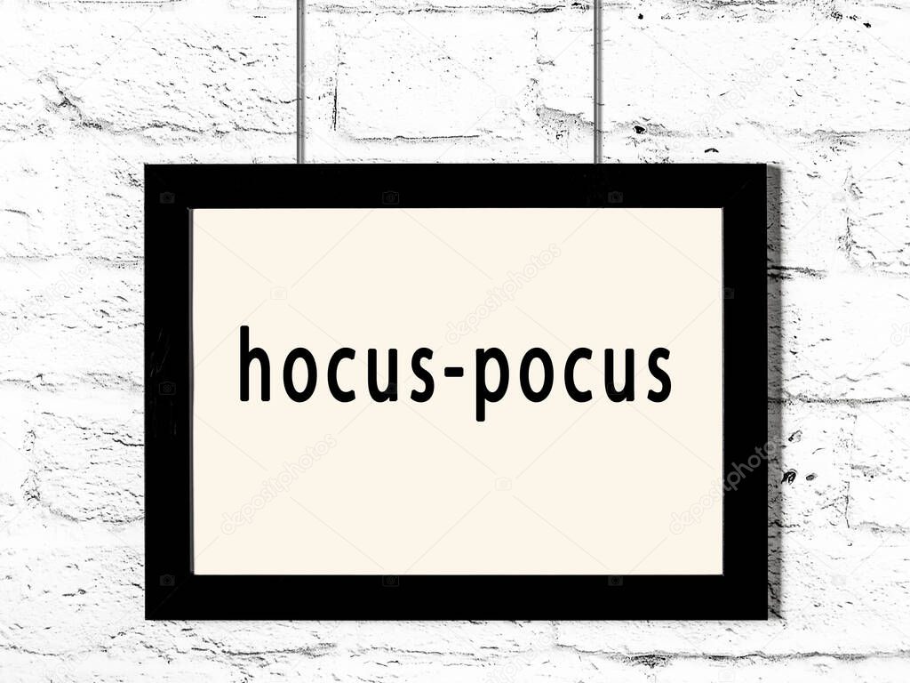 Black wooden frame with inscription hocus-pocus hanging on white brick wall 