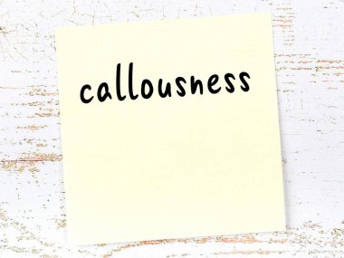 Tahta duvardaki sarı yapışkan nota, el yazısıyla yazılmış duygusuzluk.