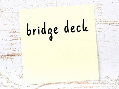 Tahta duvarda el yazısıyla yazılmış köprü güvertesi olan sarı yapışkan bir not.