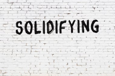 Yazı, beyaz tuğla duvara siyah boya ile yazılmış..