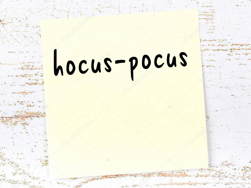 Yellow sticky note on wooden wall with handwritten inscription hocus-pocus