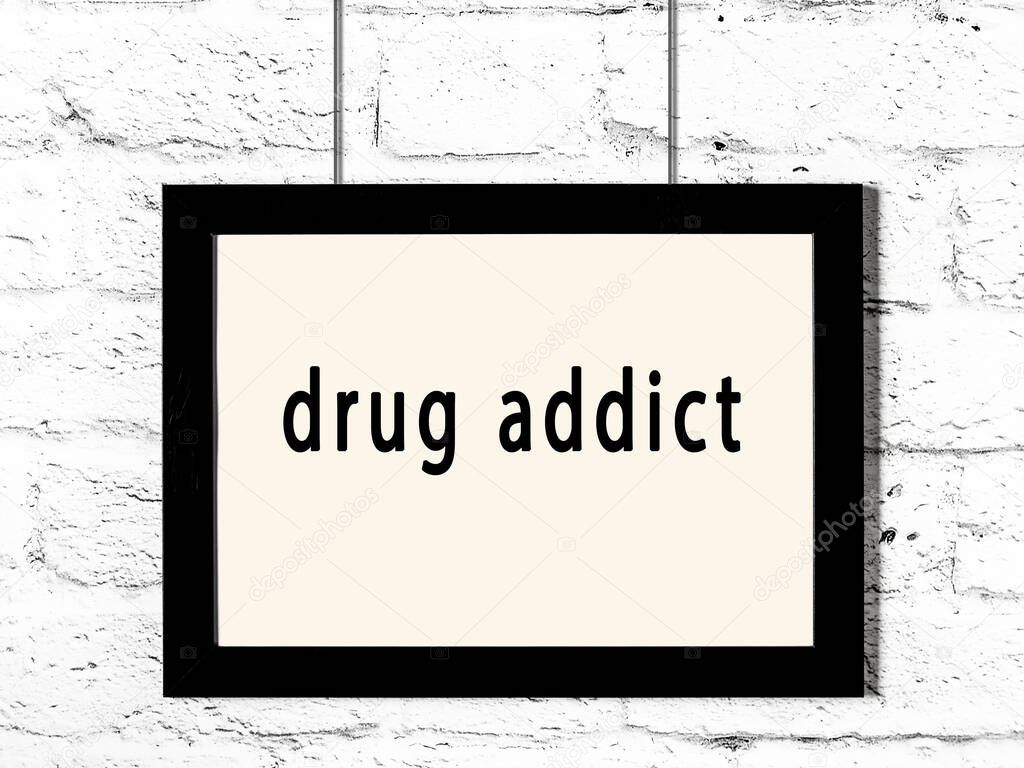 Black wooden frame with inscription drug addict hanging on white brick wall 