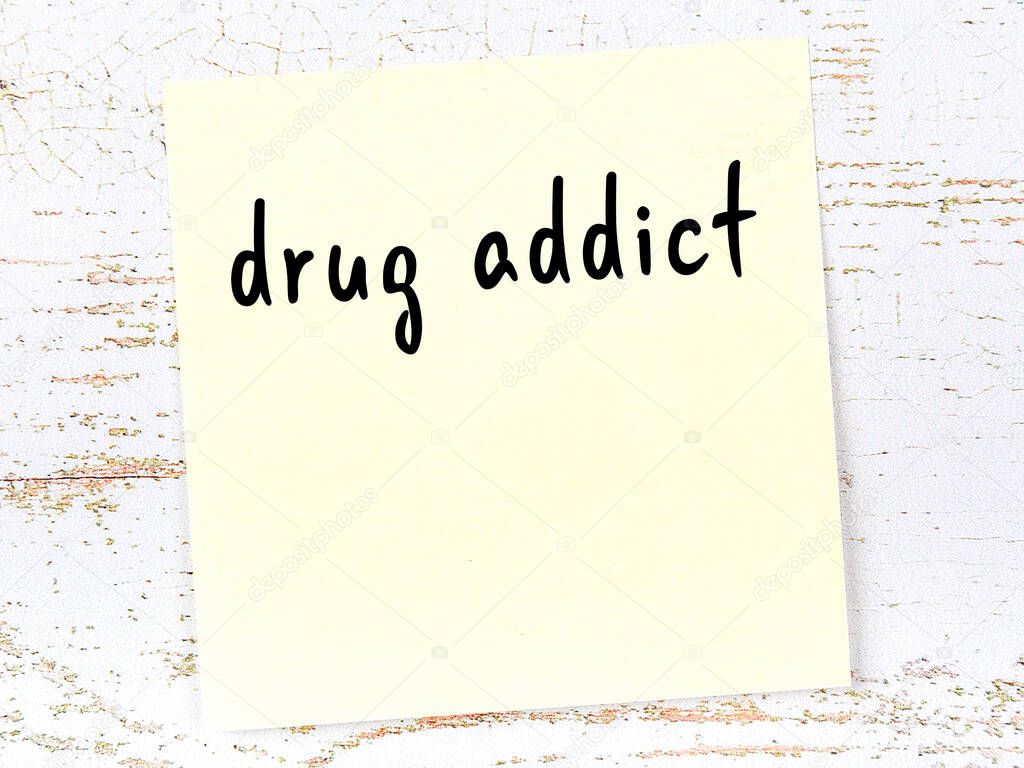 Concept of reminder about drug addict. Yellow sticky sheet of paper on wooden wall with inscription