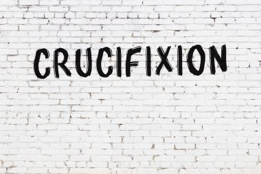 Beyaz tuğladan bir duvar. Üzerinde siyah boyayla el yazısıyla çarmıha gerilmiş.