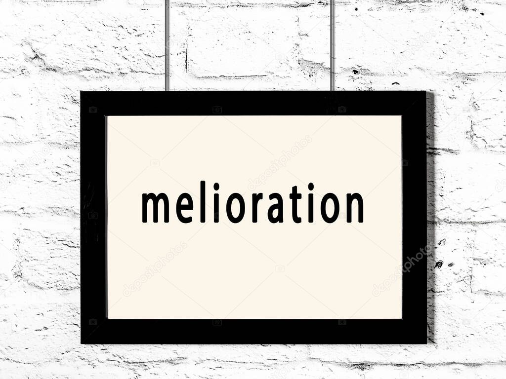 Black wooden frame with inscription melioration hanging on white brick wall 