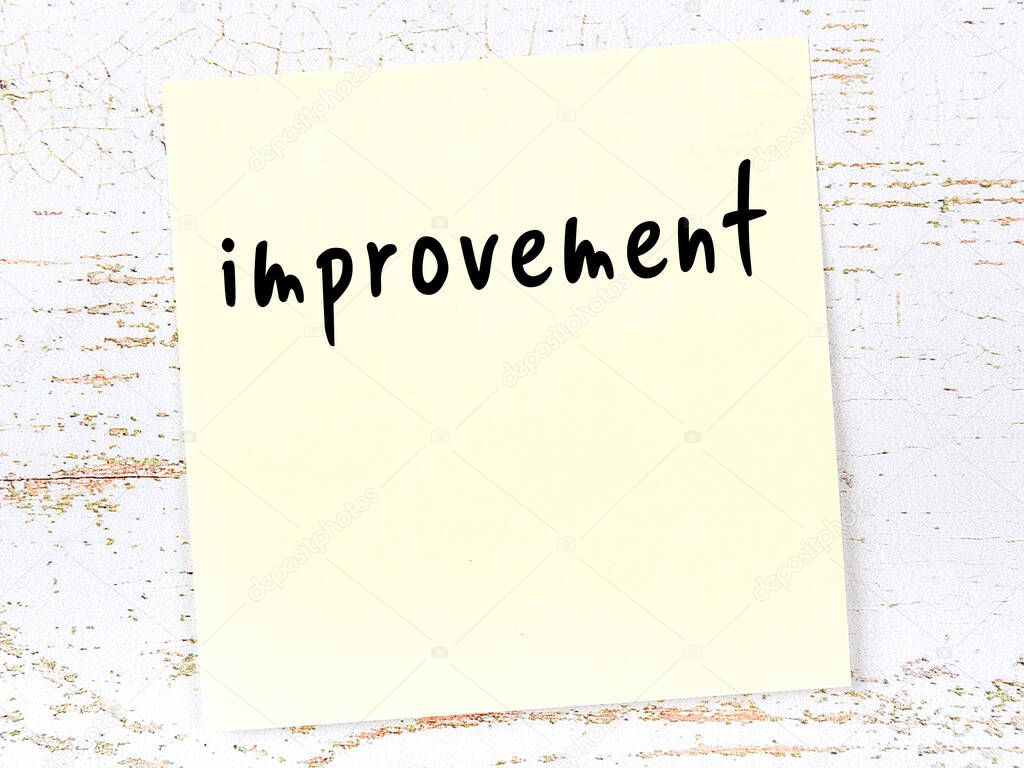 Concept of reminder about improvement. Yellow sticky sheet of paper on wooden wall with inscription