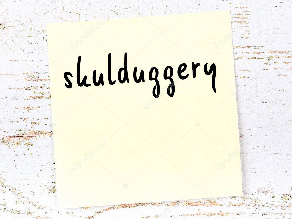 Concept of reminder about skulduggery. Yellow sticky sheet of paper on wooden wall with inscription