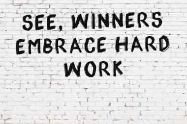 Beyaz tuğla duvara zekice alıntılar yazılı siyah bir yazı.