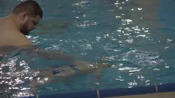 Ο γυμναστής μαθαίνει στο παιδί να κολυμπάει στην πισίνα. — Αρχείο Βίντεο