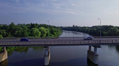 Nehir boyunca köprü, yeşil çimenler ve ağaçların etrafındaki köprüde bir sürü araba sürüyor.
