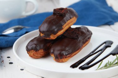 Güzel, leziz Fransız eklerleri, beyaz tabakta orijinal krema dekoru, ahşap arka planda, lezzetli renkli tatlı profiterolleri.