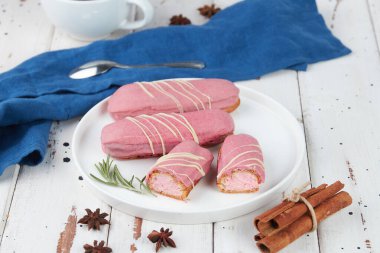 Güzel, leziz Fransız eklerleri, beyaz tabakta orijinal krema dekoru, ahşap arka planda, lezzetli renkli tatlı profiterolleri.