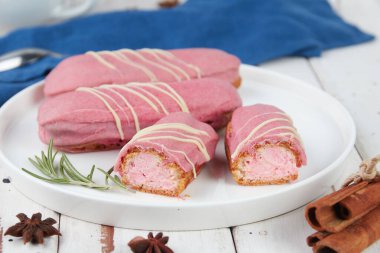 Güzel, leziz Fransız eklerleri, beyaz tabakta orijinal krema dekoru, ahşap arka planda, lezzetli renkli tatlı profiterolleri.