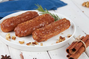 Güzel, leziz Fransız eklerleri, beyaz tabakta orijinal krema dekoru, ahşap arka planda, lezzetli renkli tatlı profiterolleri.