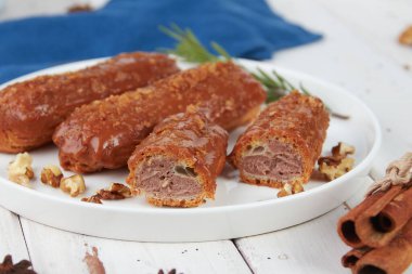 Güzel, leziz Fransız eklerleri, beyaz tabakta orijinal krema dekoru, ahşap arka planda, lezzetli renkli tatlı profiterolleri.