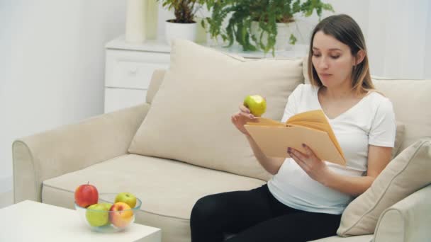 4k video van zwangere vrouw het lezen van een boek en het eten van een appel. — Stockvideo