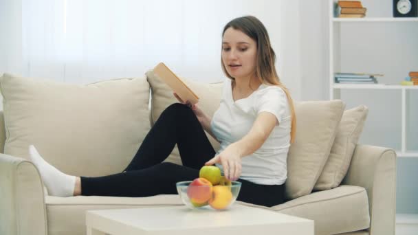 4k video de la mujer embarazada leyendo un libro y comiendo una manzana. — Vídeo de stock