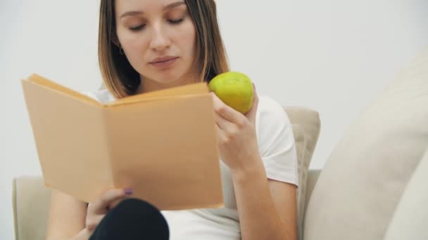 4k video av gravida kvinna läser en bok och äter ett äpple. — Stockvideo