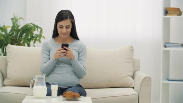 4k видео беременная женщина пьет молоко и держит телефон. — стоковое видео