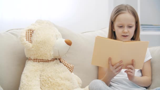 4k відео маленької дівчинки, що читає книгу своєму плюшевому ведмедику . — стокове відео