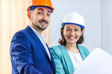 İki mühendisin kask taktığı ve elinde kağıt tutarken çekilmiş bir fotoğraf..