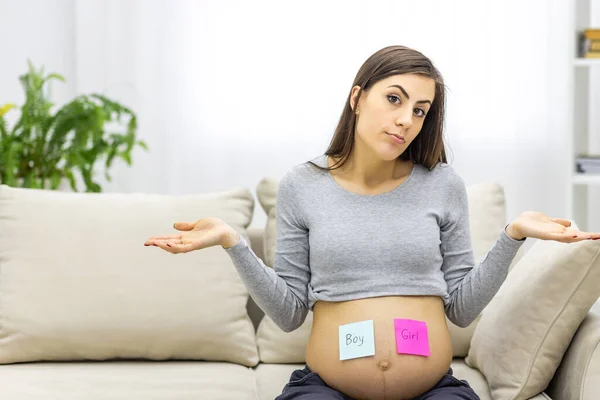 Foto de una mujer embarazada sosteniendo papeles rosas y azules que significan el género del futuro bebé. —  Fotos de Stock