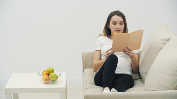 4k vídeo de mulher grávida lendo um livro e comendo uma maçã. — Vídeo de Stock