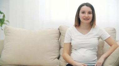 4k video 'da hamile kadın beyaz koltukta oturup karnına dokunuyor..