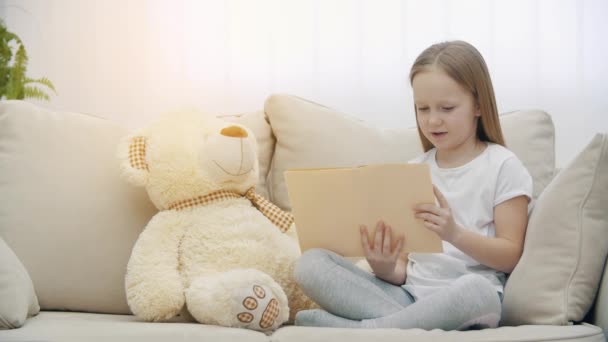 Vidéo ralenti 4k de petite fille lisant un livre à son ours en peluche. — Video