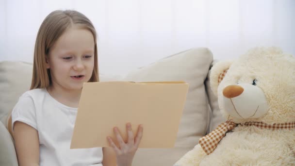 4k повільне відео маленької дівчинки, що читає книгу своєму плюшевому ведмедику . — стокове відео