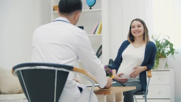 4k видео, где беременная женщина разговаривает с врачом. — стоковое видео
