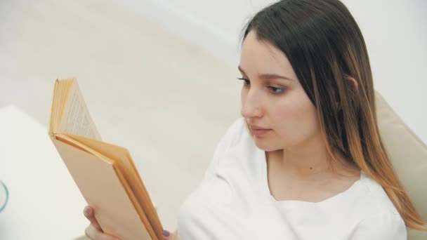 4k video de la mujer embarazada en el sofá leyendo un libro. — Vídeo de stock