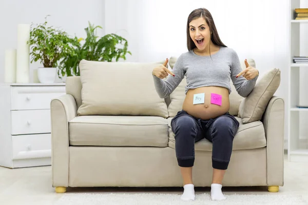 Foto einer schwangeren Frau mit rosa und blauen Papieren auf dem Bauch. — Stockfoto