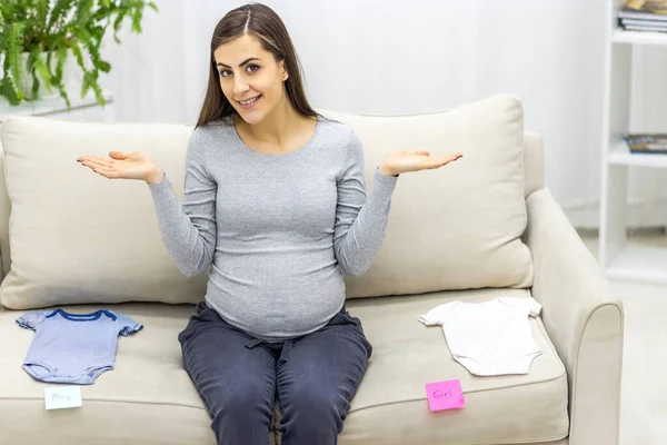 Foto einer schwangeren Frau mit Kinderkleidung auf dem Sofa. — Stockfoto