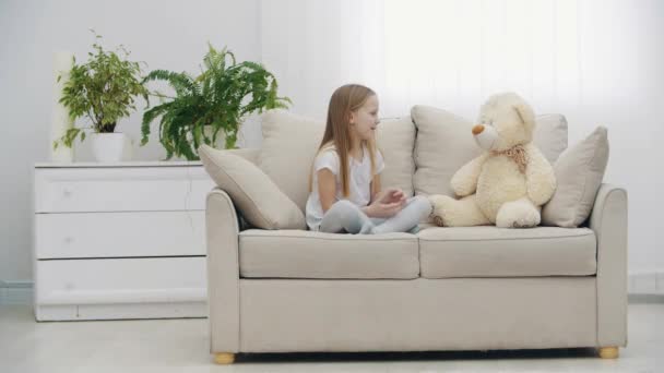 4k videó a fehér ruhás kislányról, aki Teddy macival beszél. — Stock videók