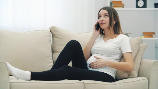 4k-Video von schwangerer Frau, die auf weißem Sofa telefoniert. — Stockvideo