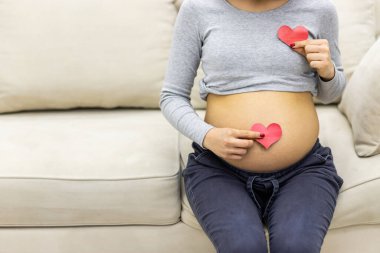 Hamile bir kadının kırmızı kalple karnının ve elinin kesilmiş fotoğrafı..