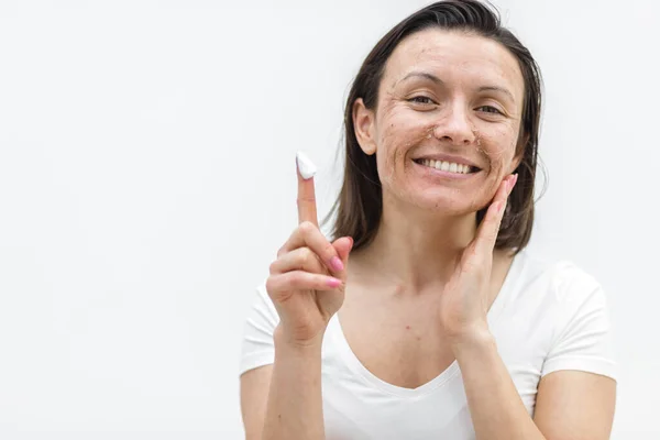Photo d'une femme souriante à la peau sèche montrant un doigt dans une crème. — Photo