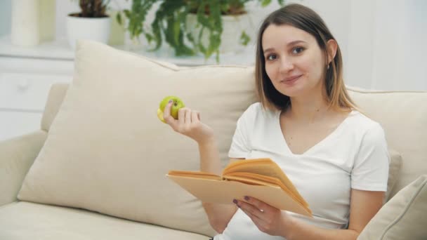 4k video van zwangere vrouw het lezen van een boek en het eten van een appel. — Stockvideo
