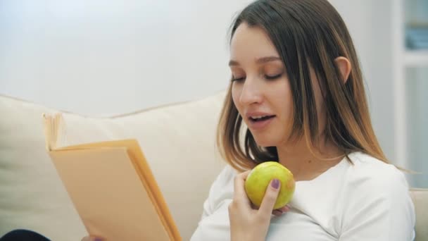 4K yakın çekim videosunda hamile bir kadın yeşil elmalı bir kitap okuyor.. — Stok video