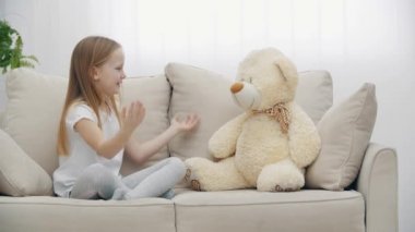 Beyaz elbiseli küçük bir kızın oyuncak ayıyla konuştuğu 4K video..