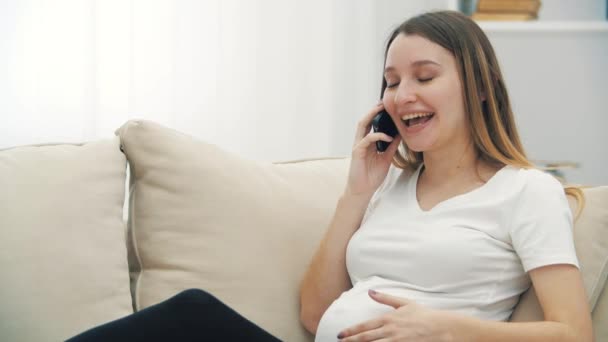 4k video av gravida kvinna talar över telefon på vit soffa. — Stockvideo